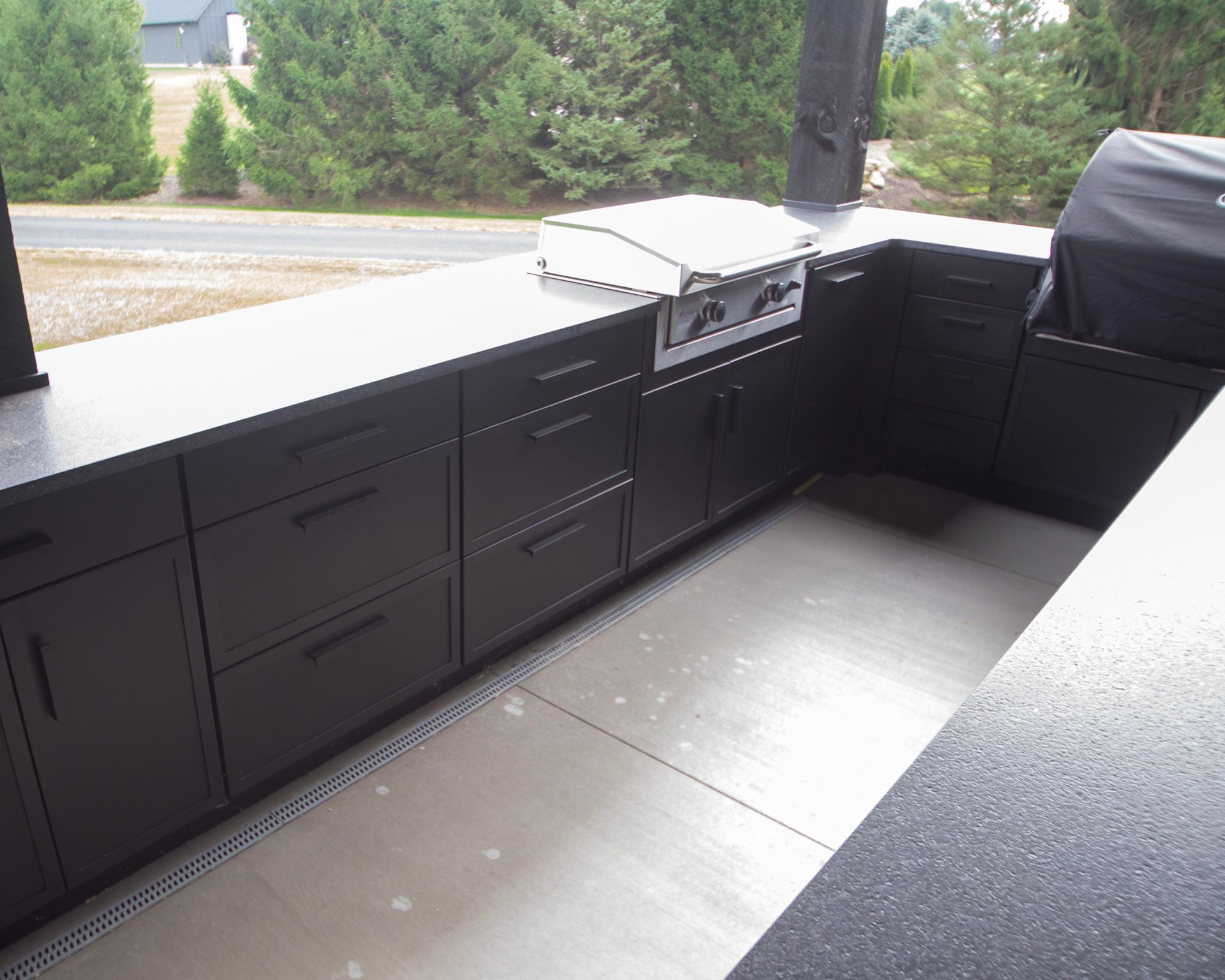 Outdoor kitchen with dark cabinets, built-in grill, and light gray counter on a covered patio