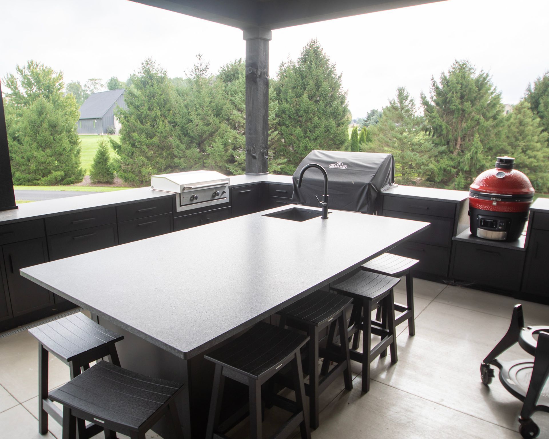 Covered patio with a black dining table, stools, grill, and green backyard view