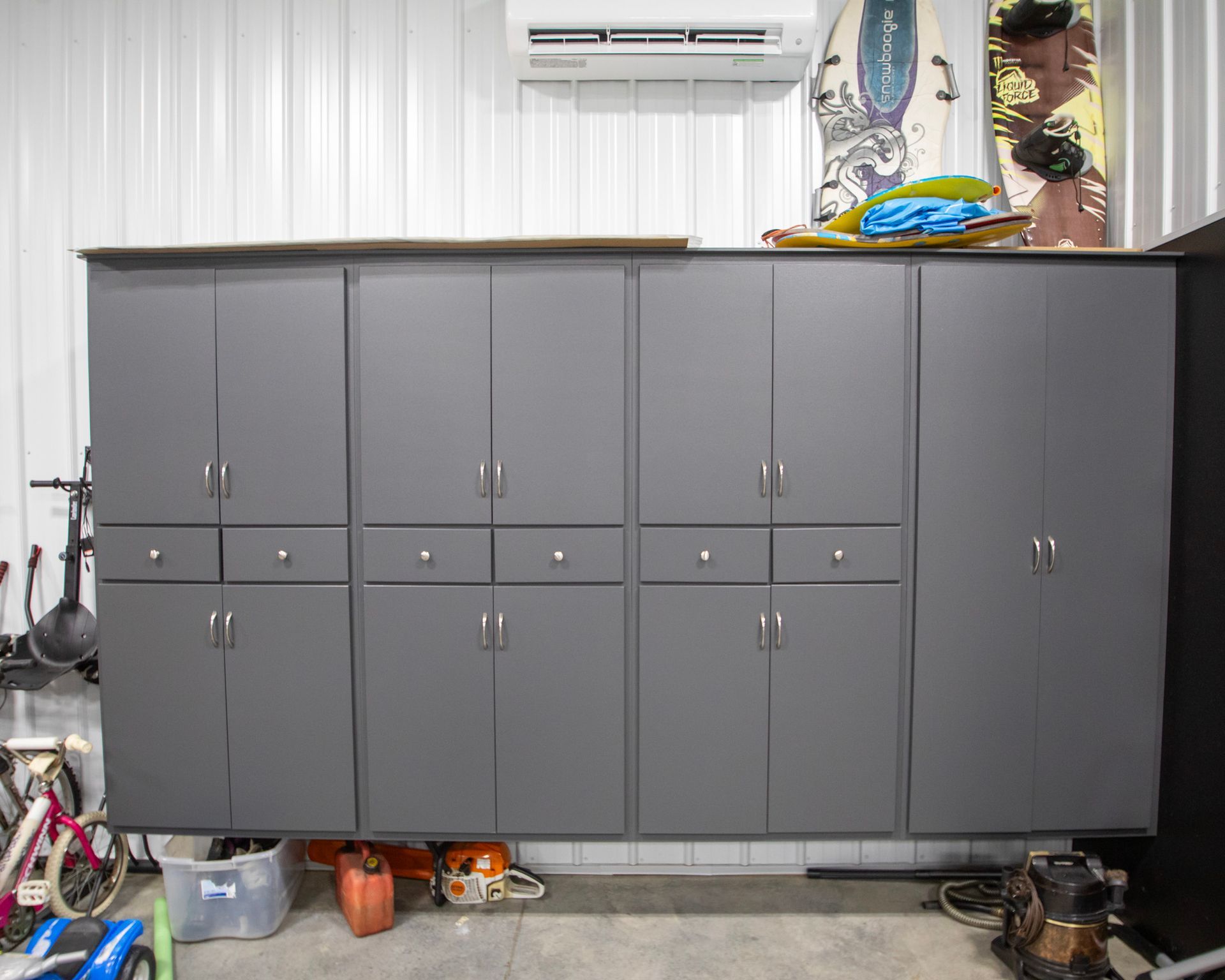 Gray storage cabinets against a white wall in a garage, with tools and a bicycle partially visible.