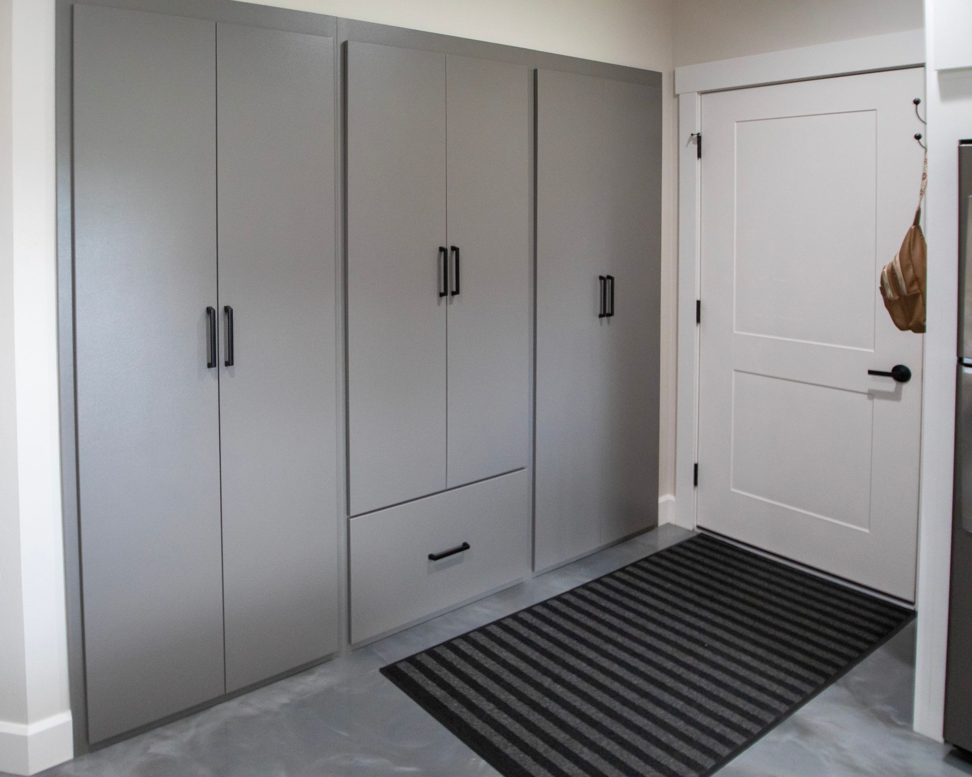 Gray built-in cabinets beside a white door in a small entryway with a striped rug