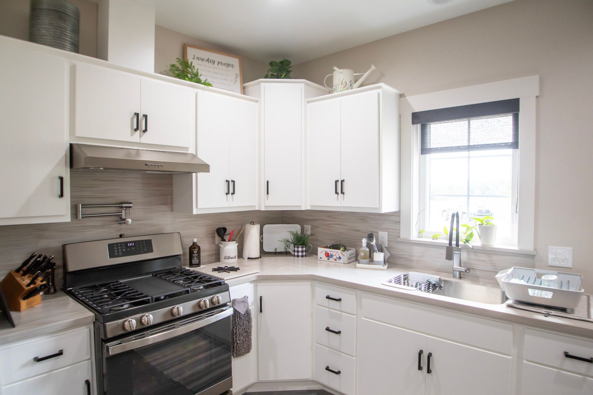 Bright white kitchen with stainless stove, corner cabinets, and a sunlit window over the sink.