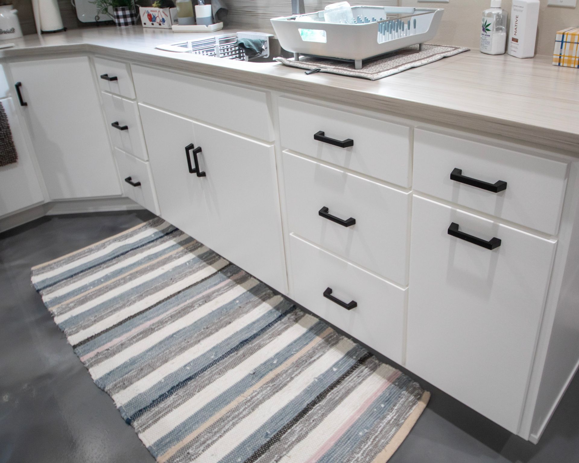 White bathroom vanity with black hardware, striped rug, and countertop toiletries