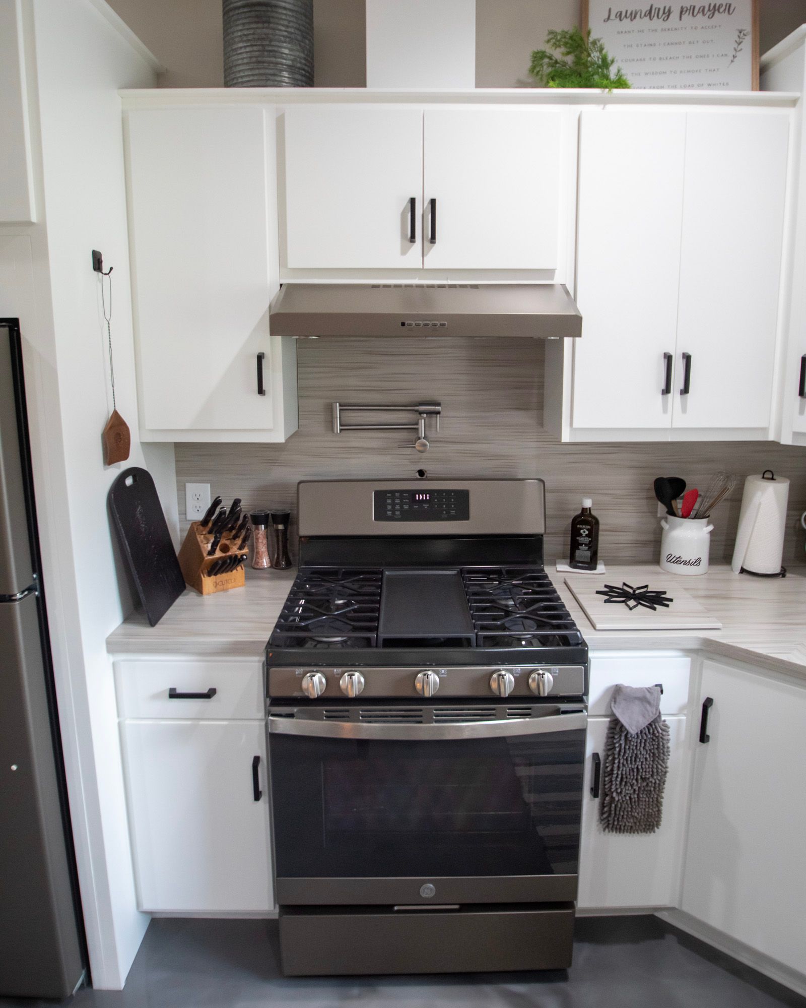 Compact white kitchen with stainless steel gas range, white cabinets, and gray tile backsplash