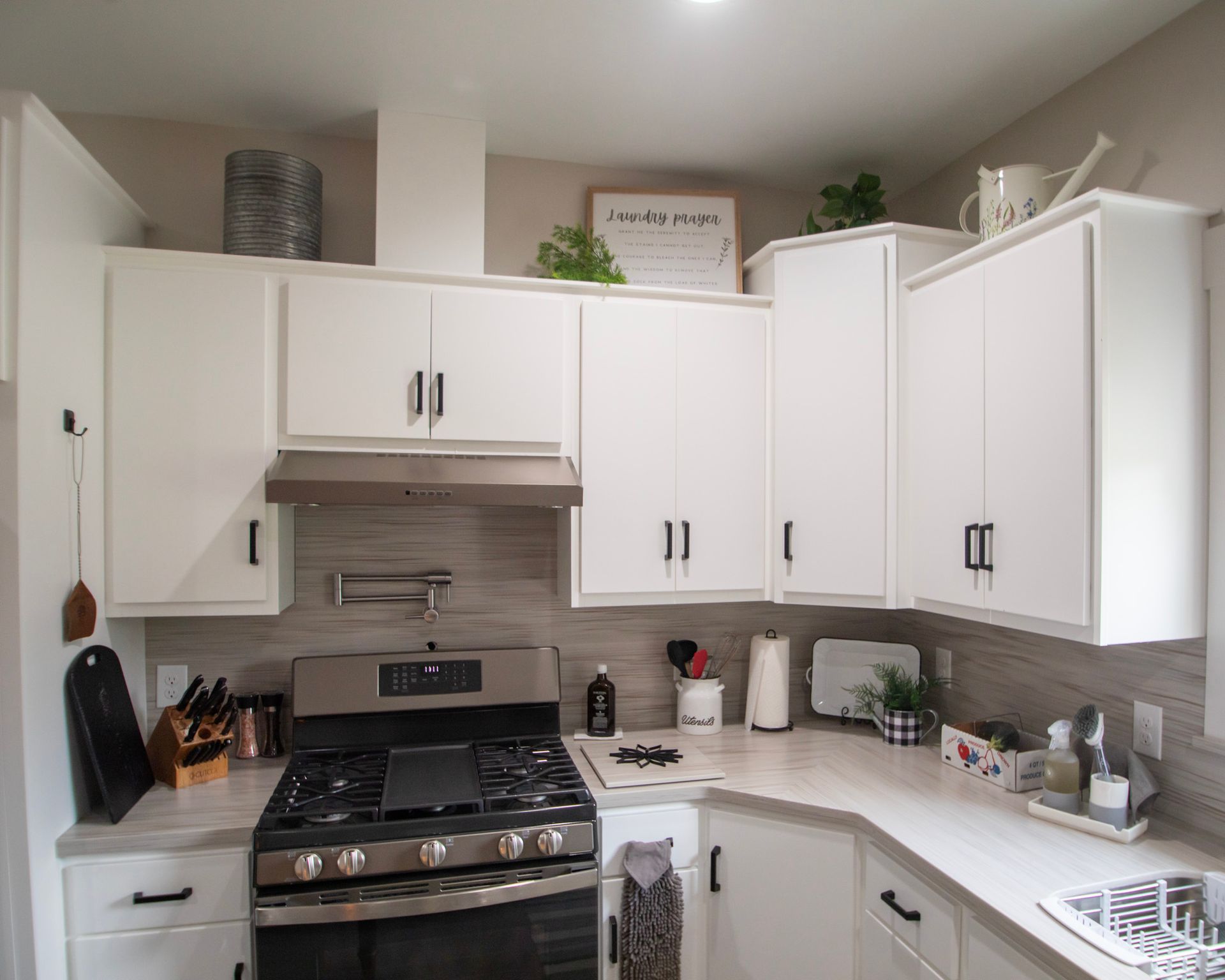 Bright white kitchen with white cabinets, black stove, and light countertops.