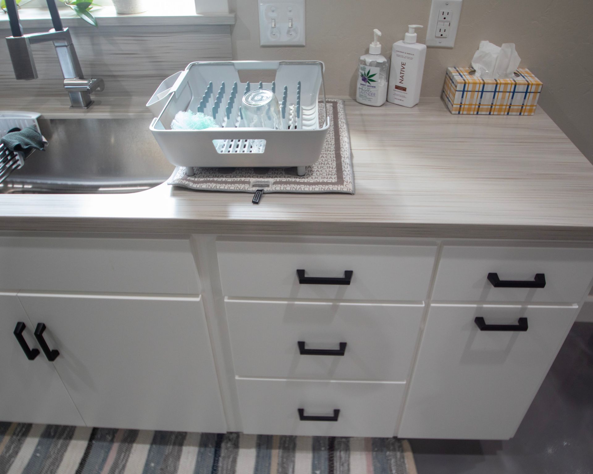 Kitchen counter with sink, dish rack, and white cabinets, viewed from above.