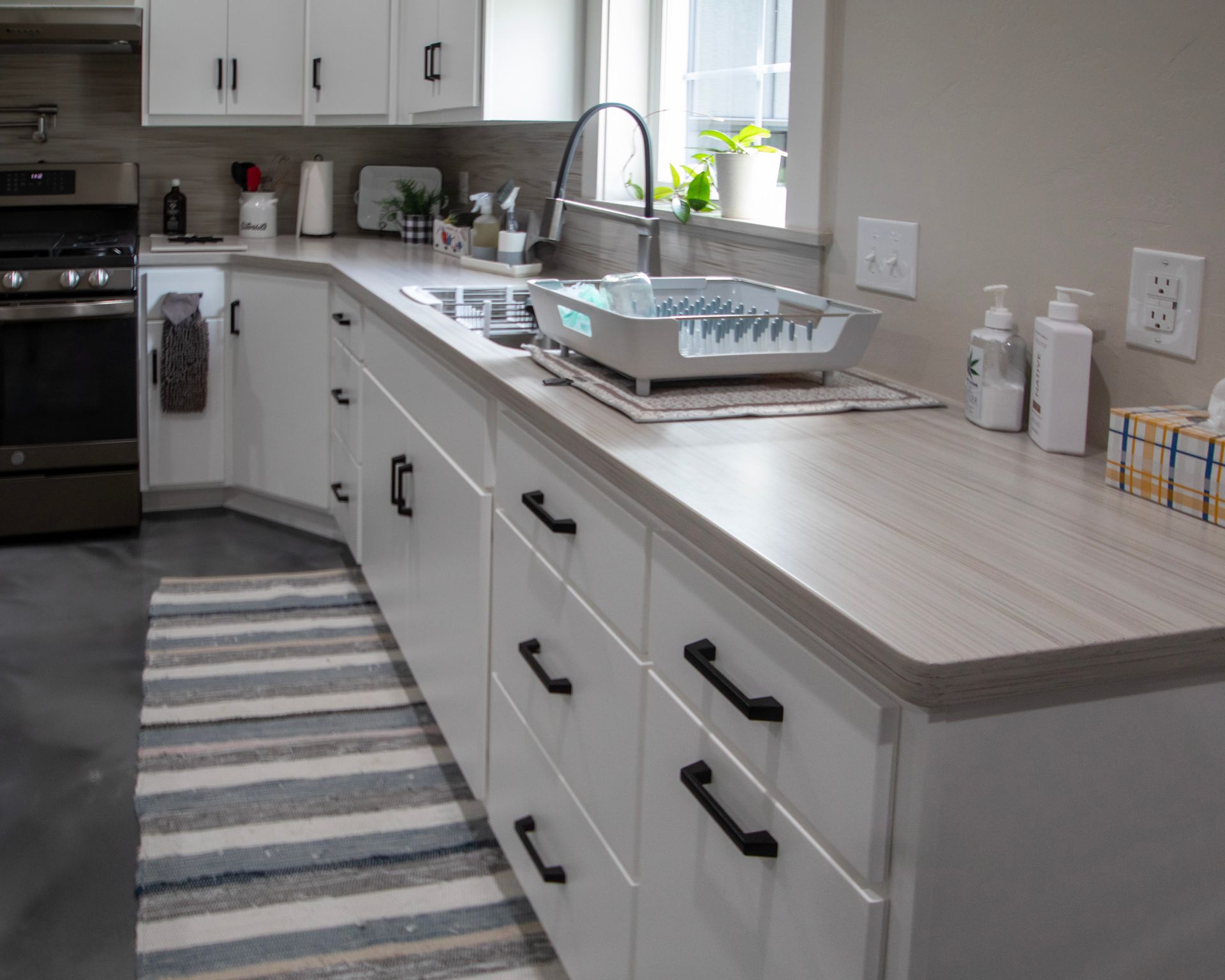 Bright modern kitchen with white cabinets, gray countertop, sink, and striped runner rug