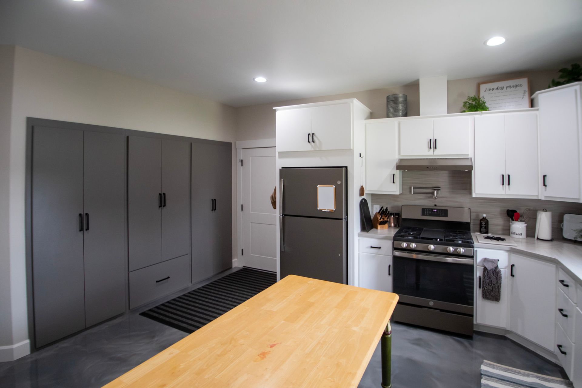 Modern kitchen with white and gray cabinets, stainless fridge and stove, and a wooden island in the foreground
