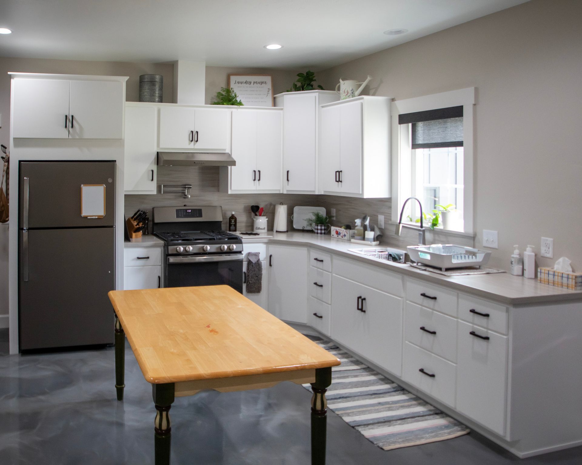 Bright modern kitchen with white cabinets, stainless fridge, and a wooden table in the center