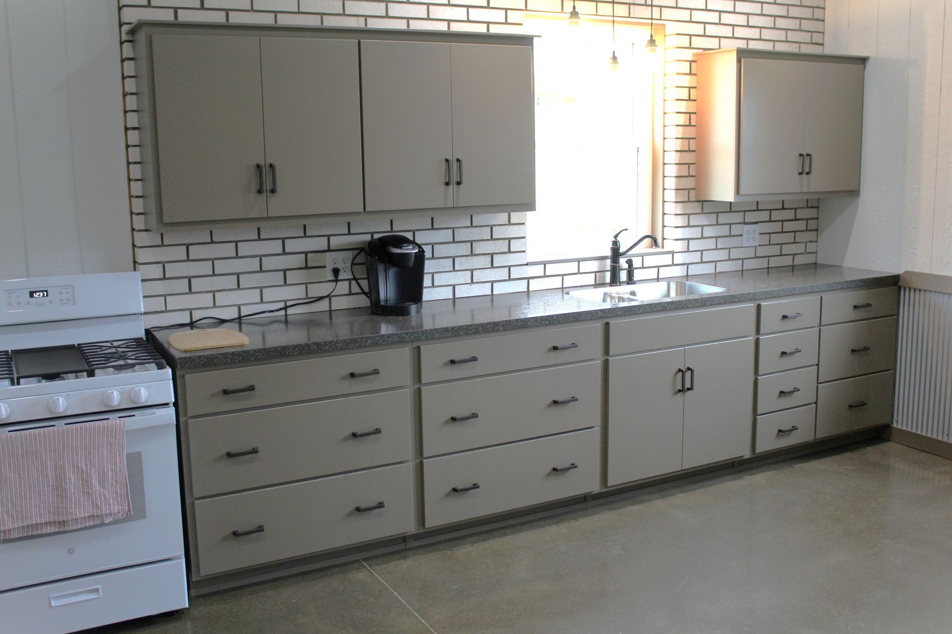 Empty kitchen with gray cabinets, white subway tile backsplash, stove, and coffee maker on the counter