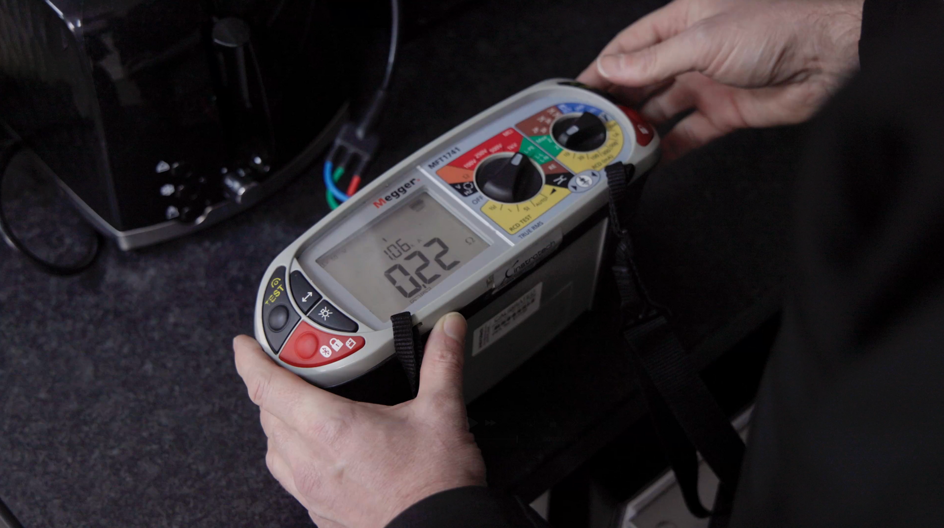 Hands hold a multi-function electrical tester showing a reading of 0.22 on its digital display.