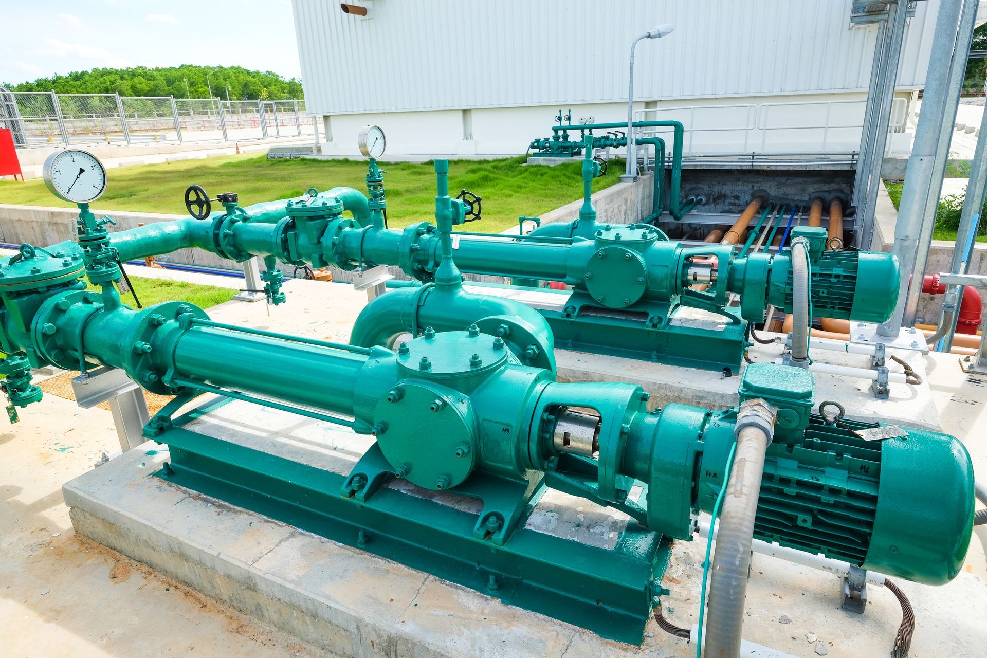 Green industrial pumps and pipes installed outdoors beside a large building.