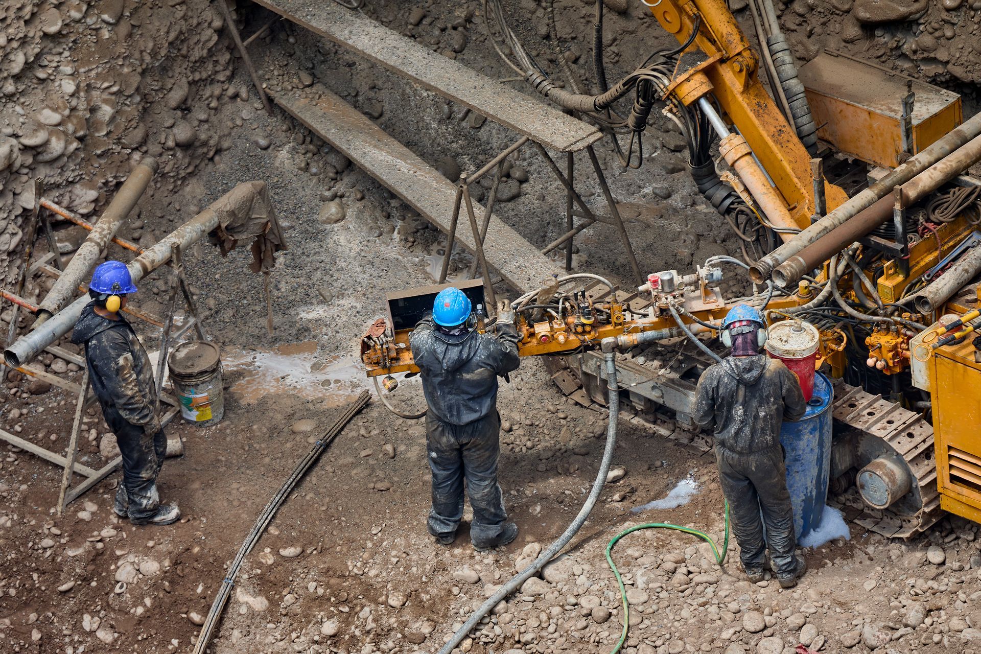 Workers in hard hats operating heavy drilling equipment at a construction site
