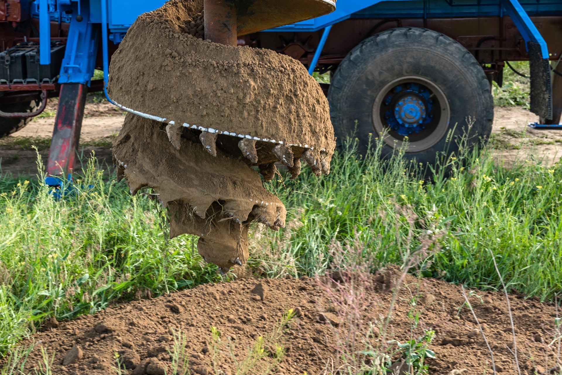 Tractor attachment dropping clods of soil onto a grassy field beside a blue vehicle