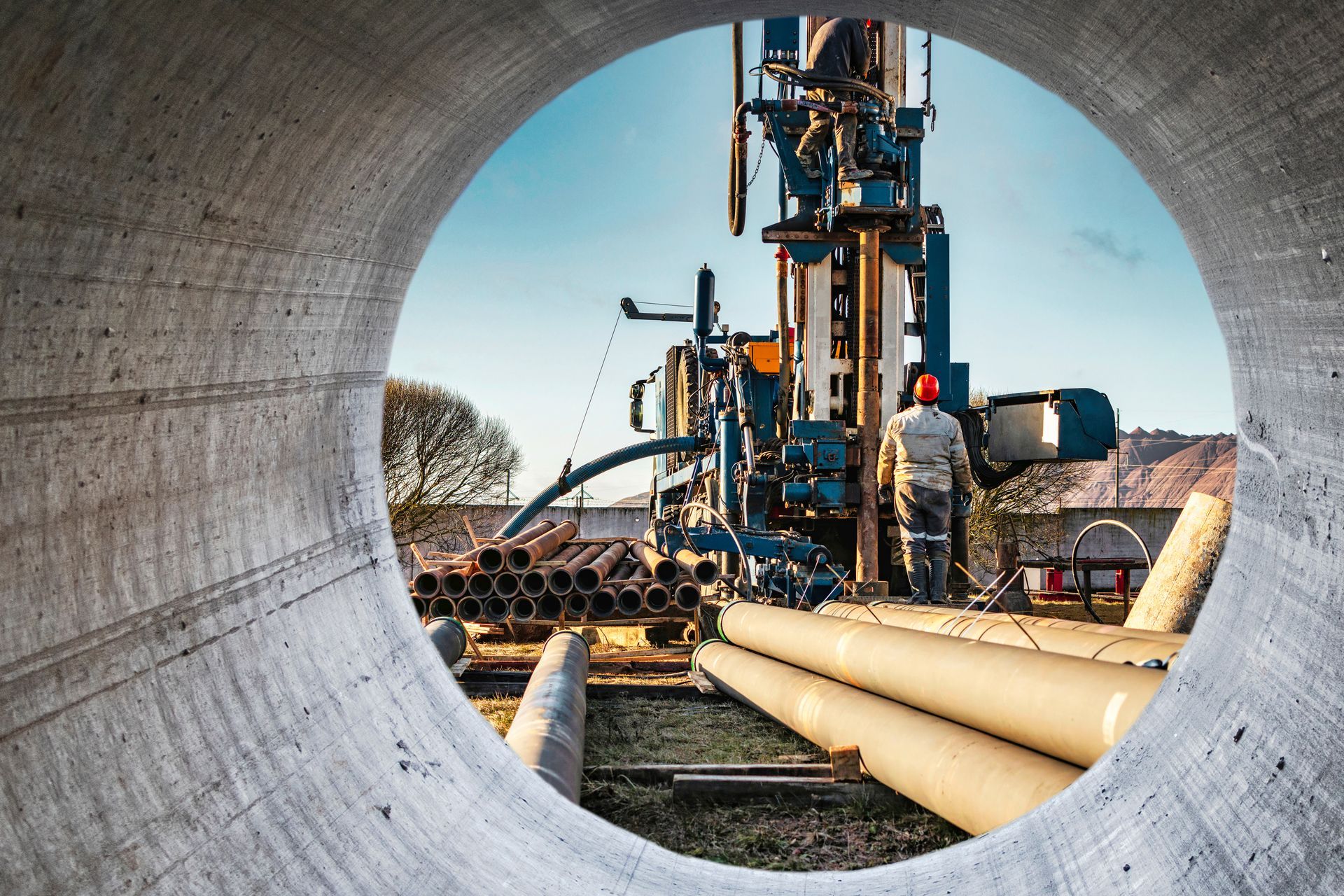Pipeline workers and drilling rig viewed through a large concrete pipe opening