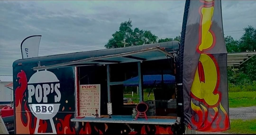 Bright pink food truck with neon burger logo and menu parked outdoors in the sun.