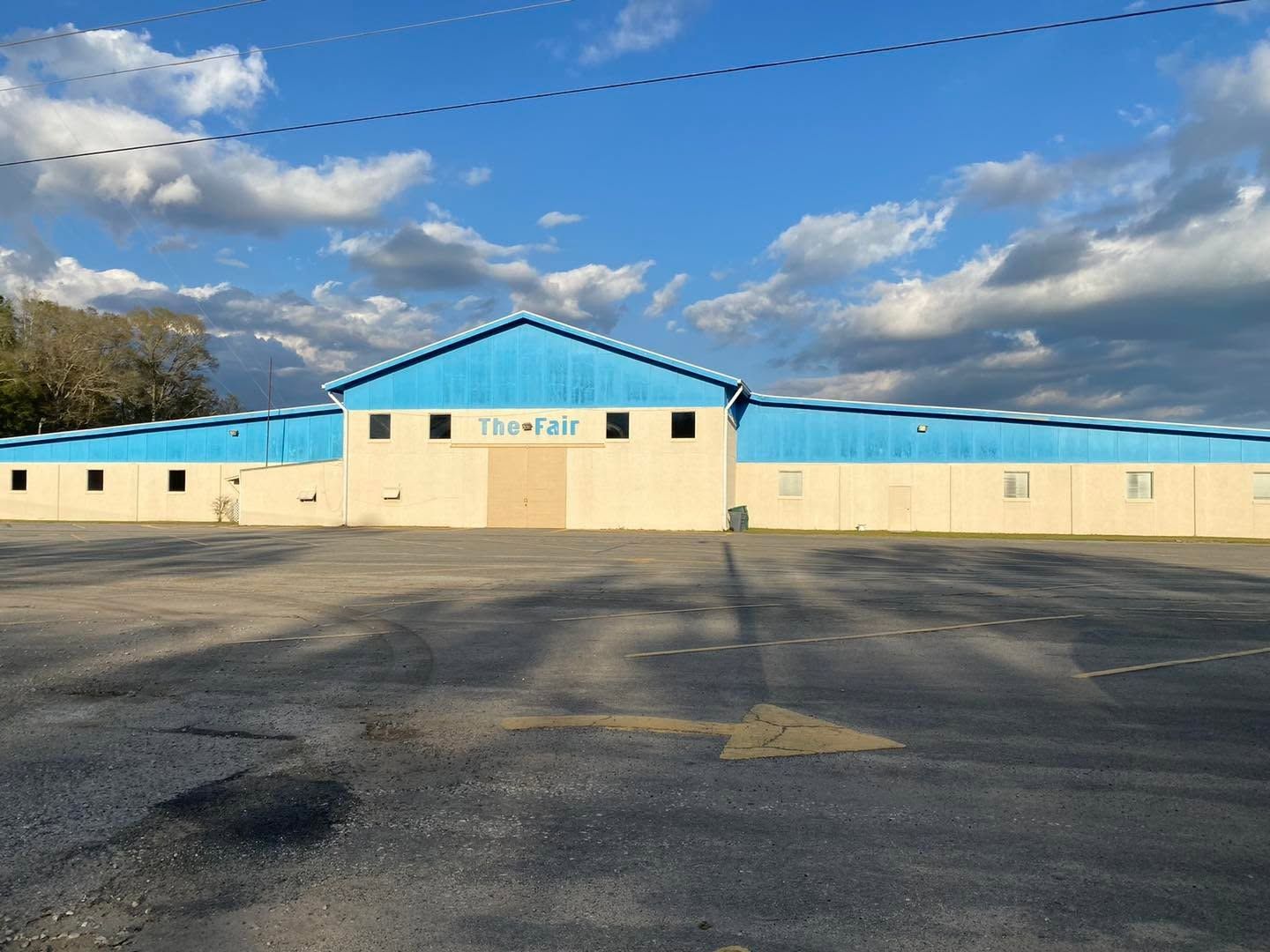 Single-story beige building with a blue roof and empty parking lot under a cloudy sky