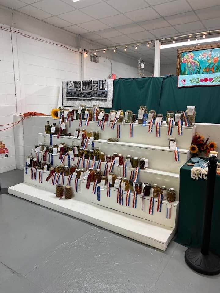 Display of colorful handmade crafts on white shelves in a booth with green curtains and gray floor