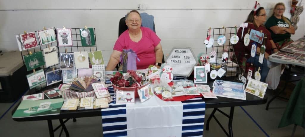 Vendor table with handmade crafts, cards, and trinkets displayed at an indoor fair booth