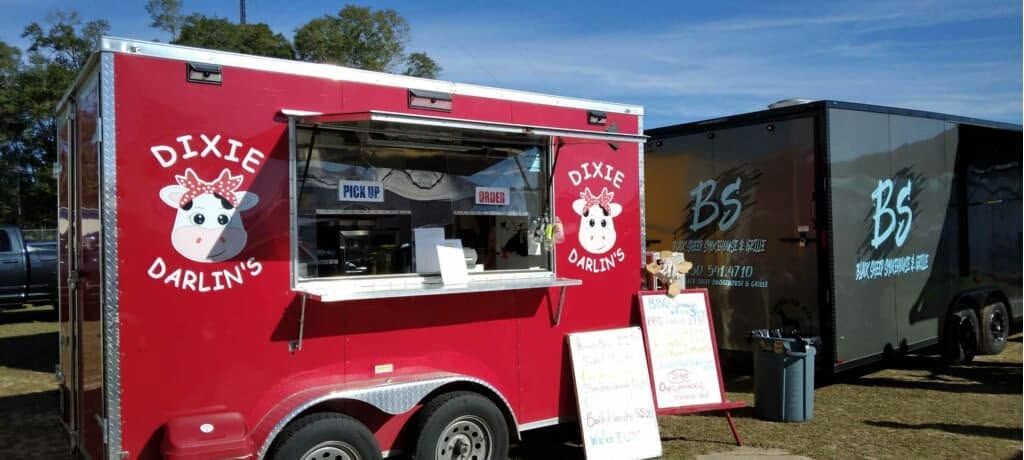 Red Dixie Darling food truck with serving window beside a black trailer at an outdoor event.