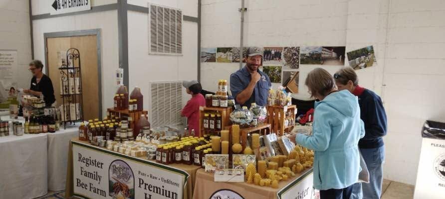 People browsing a honey and jam stall at an indoor market booth