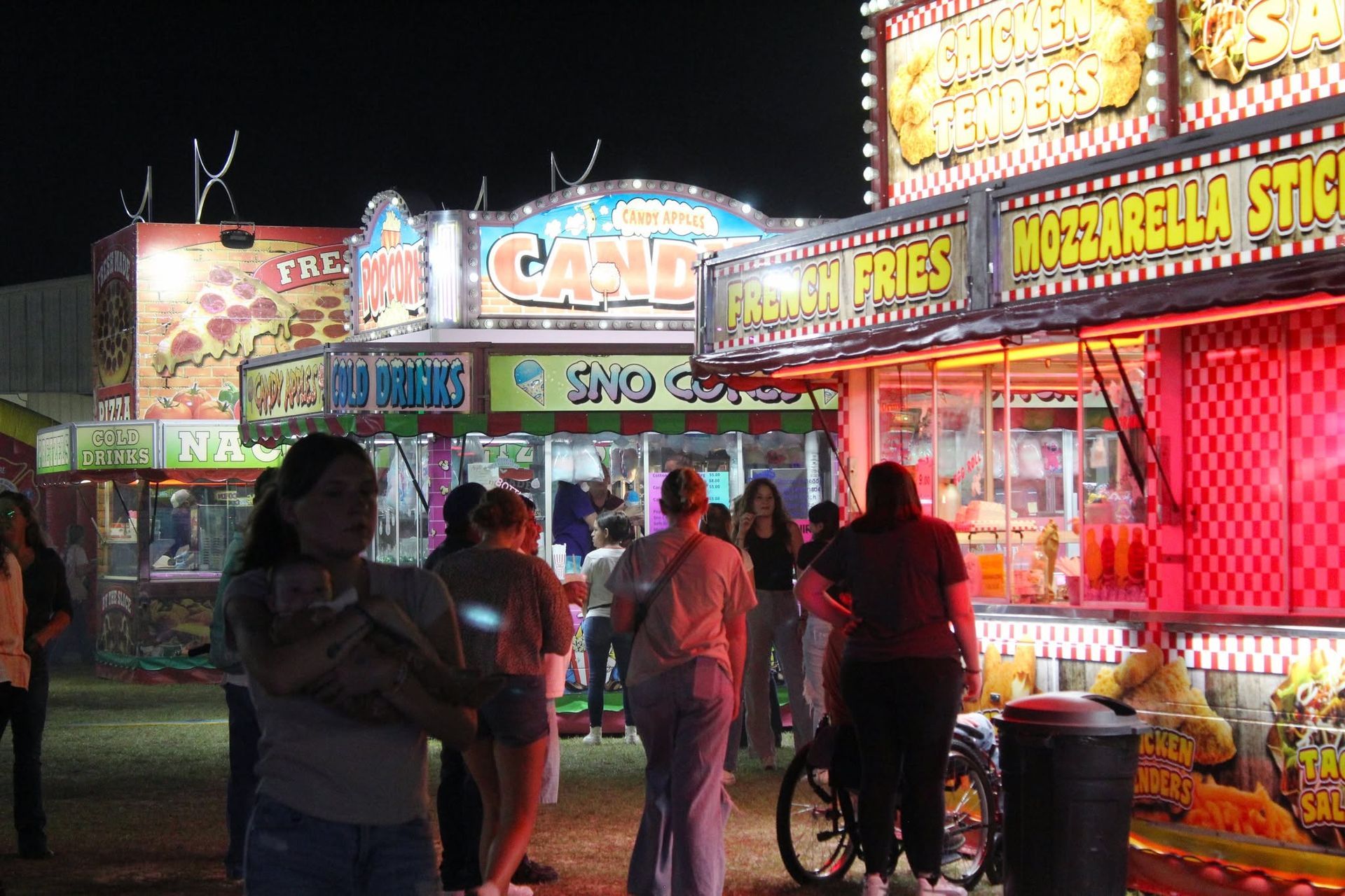 Nighttime fair food stand with neon signs and people waiting in line