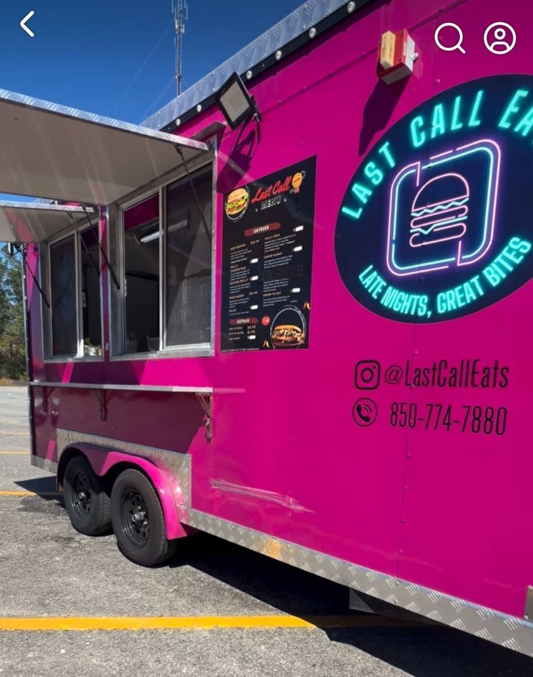 Bright pink food truck with neon burger logo and menu parked outdoors in the sun.