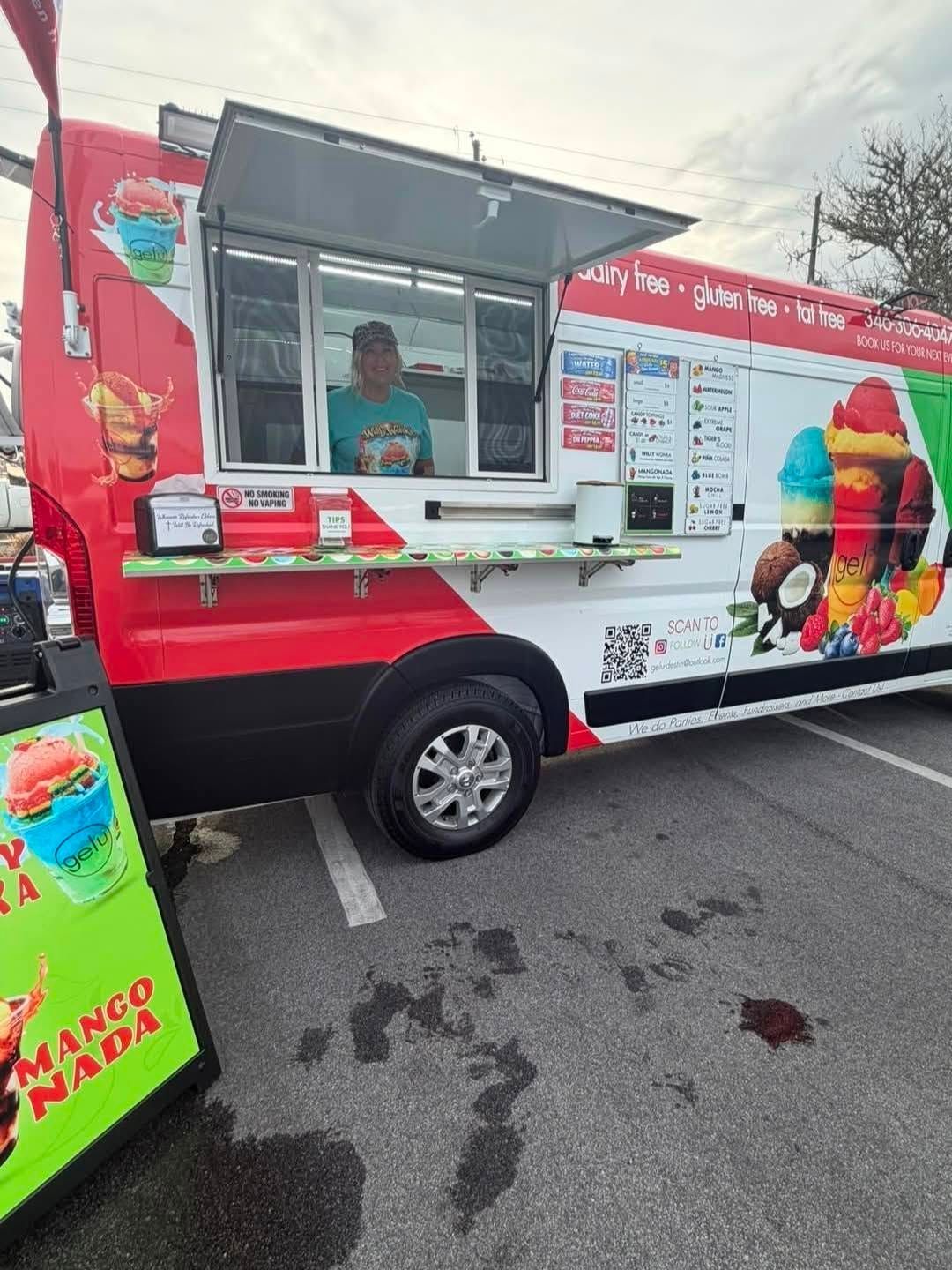 Red and white ice cream truck with vendor at serving window in a parking lot.
