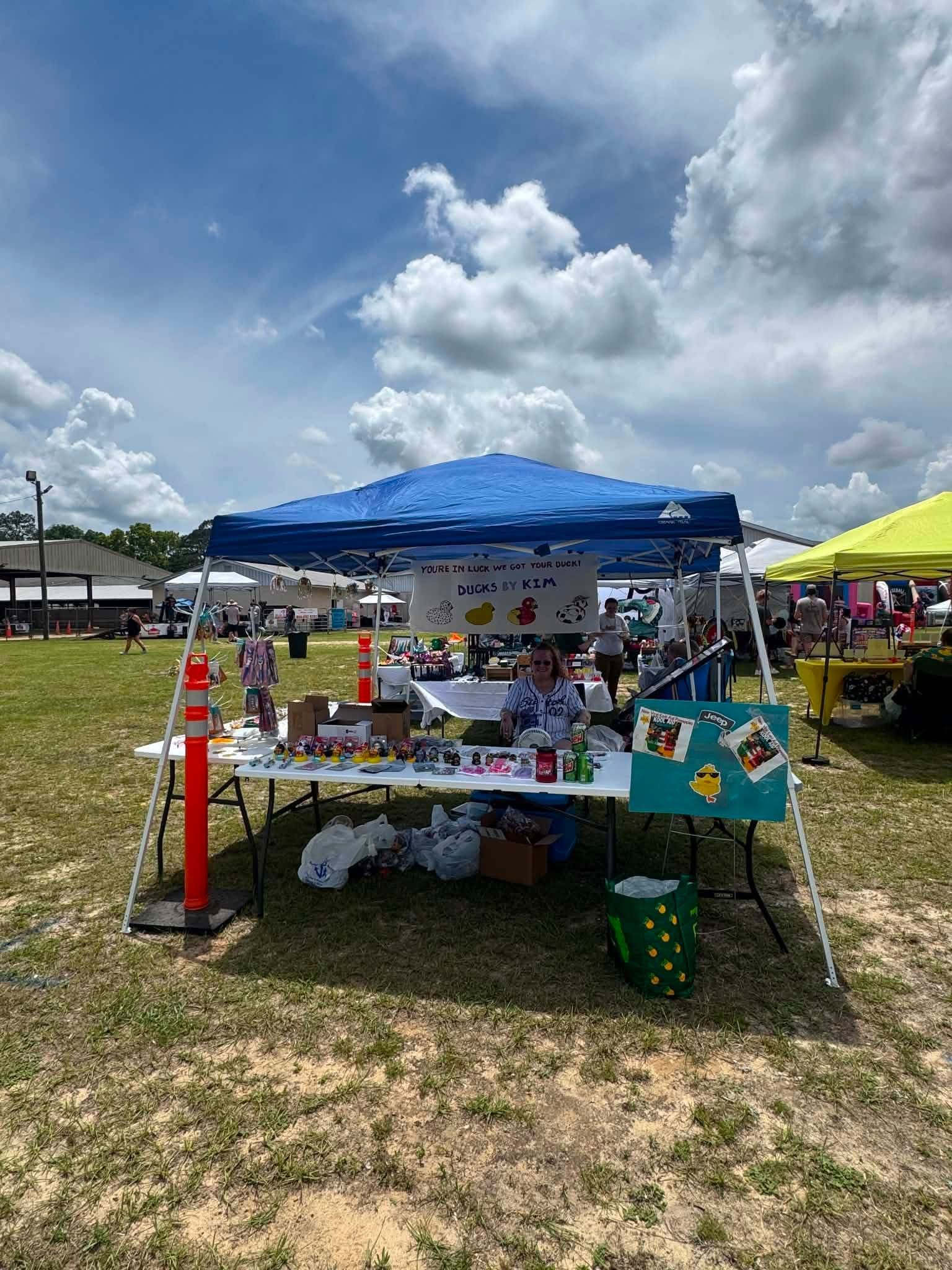 Vendor booth with blue canopy and colorful displays at an outdoor fair under a cloudy sky