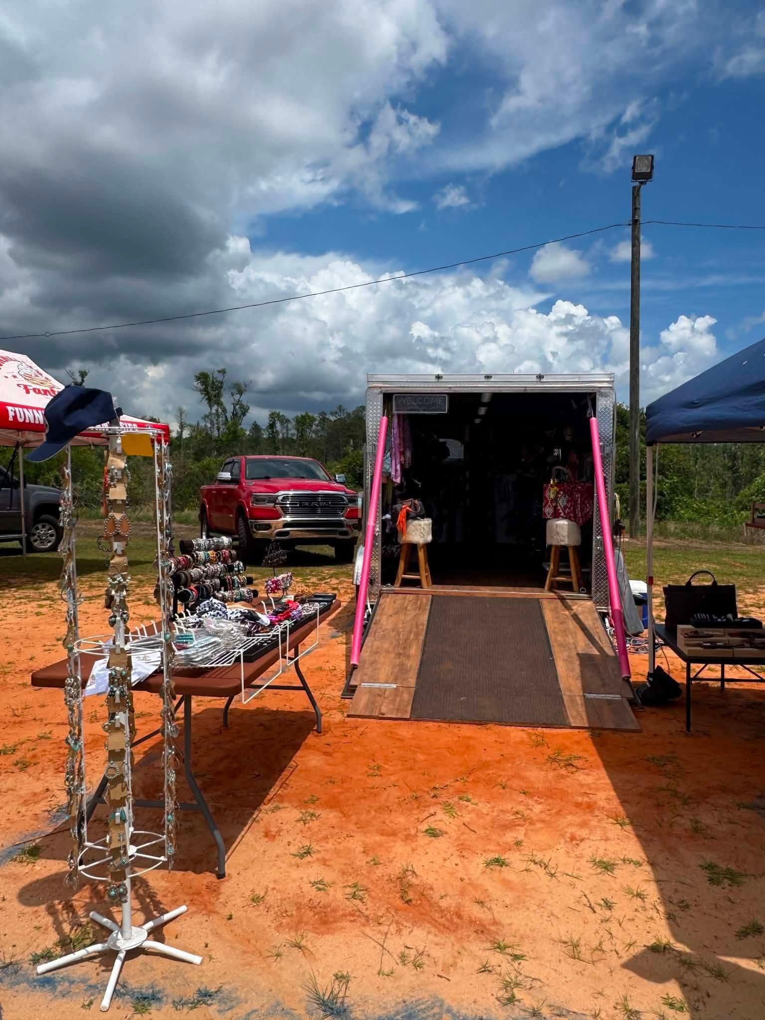 Outdoor event setup with tables, tents, and a pink trailer on a muddy field under a cloudy sky