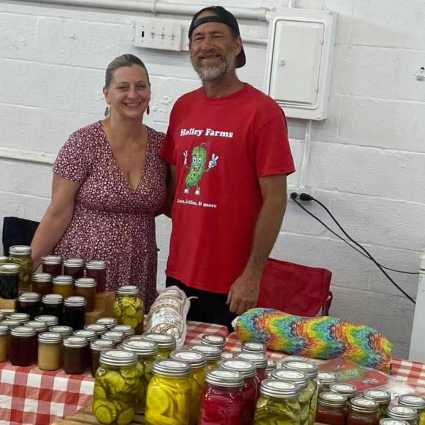 Table of baked goods at a market stall with two vendors behind it and a holiday wreath backdrop