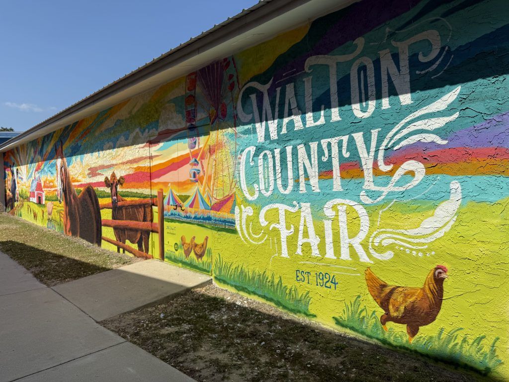 Colorful mural on a building reading “Walton County Fair” with a rooster and fence scene