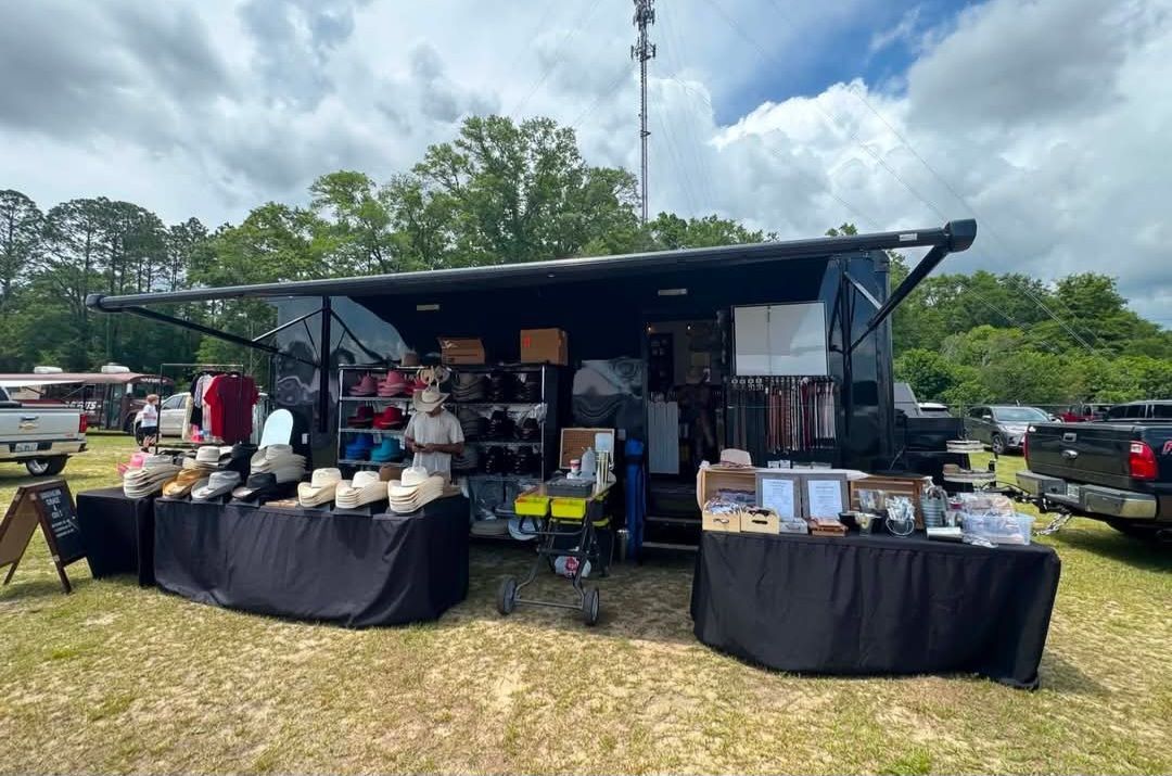 Outdoor market stall with tables of jars and packaged goods under a black canopy in a grassy field