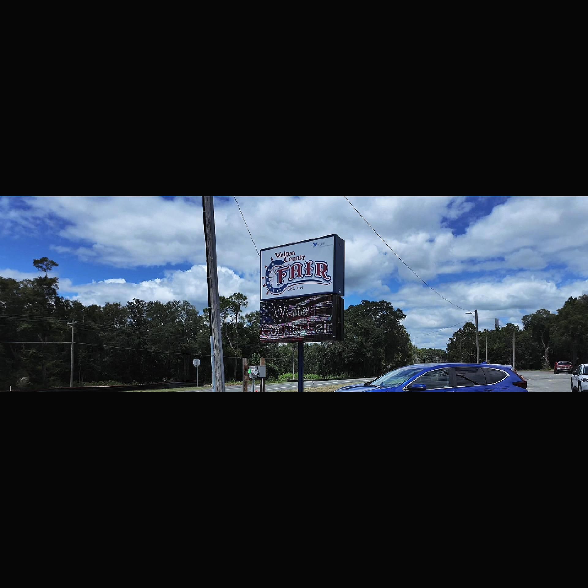 Roadside sign under a cloudy sky with a blue car passing by.