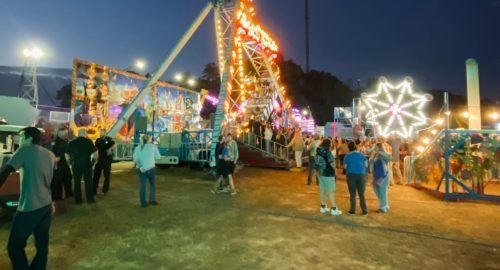 Night carnival with colorful rides, lit ferris wheel, and people walking on a fairground at dusk
