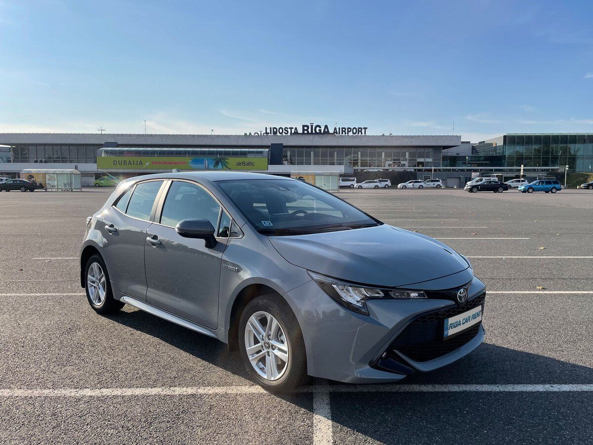 Toyota Corolla ir novietota stāvvietā ēkas priekšā.