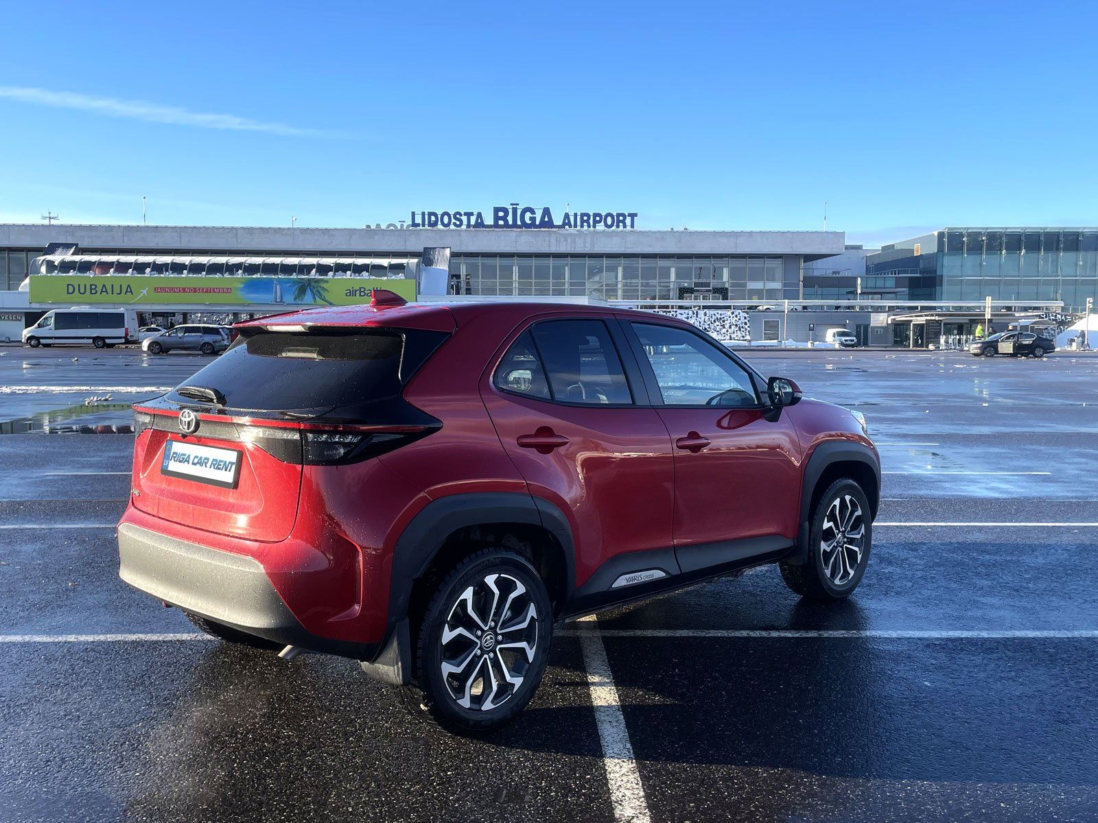 Sarkana automašīna ir novietota stāvvietā lidostas priekšā.