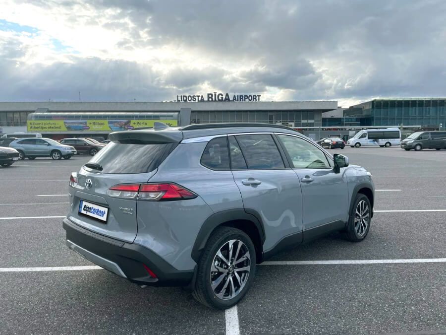 Pelēka automašīna ir novietota stāvvietā lidostas priekšā.