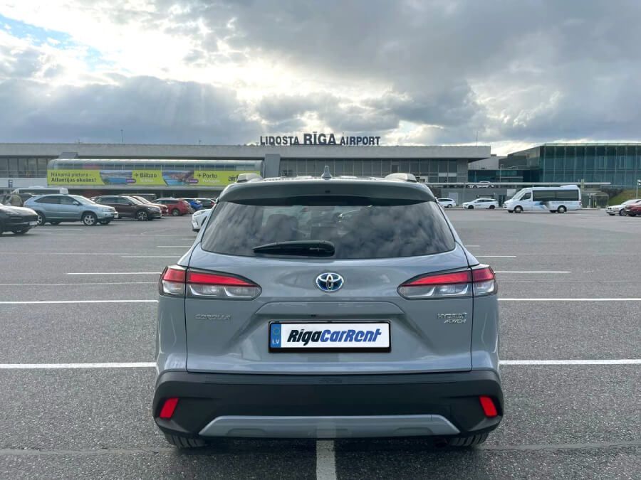 Toyota Corolla Cross ir novietota autostāvvietā lidostas priekšā.