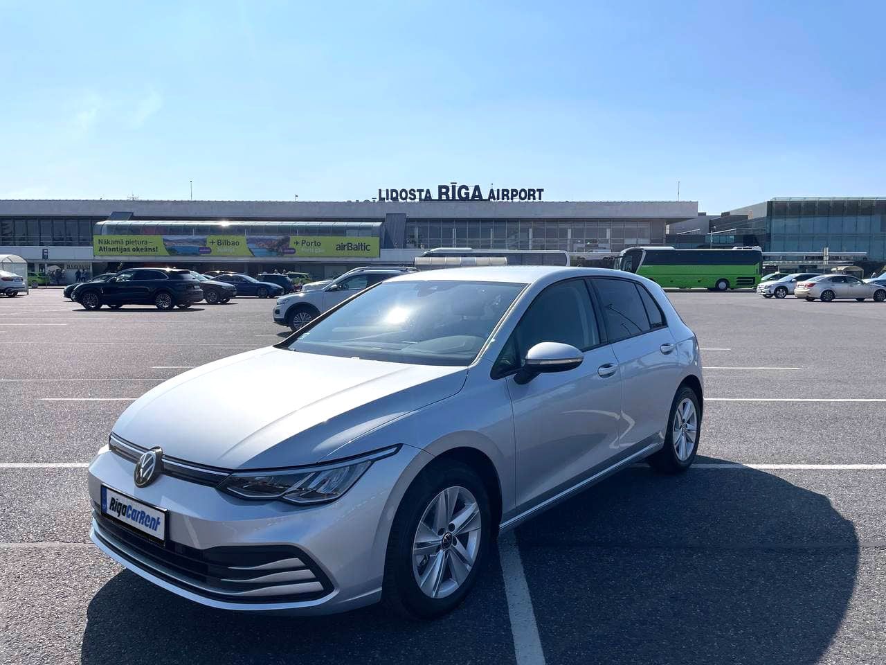 Sudraba krāsas Volkswagen Golf ir novietots autostāvvietā lidostas priekšā.