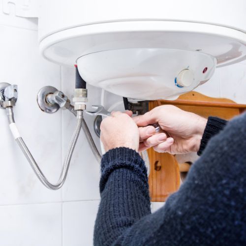 A man is fixing a water heater in a bathroom.