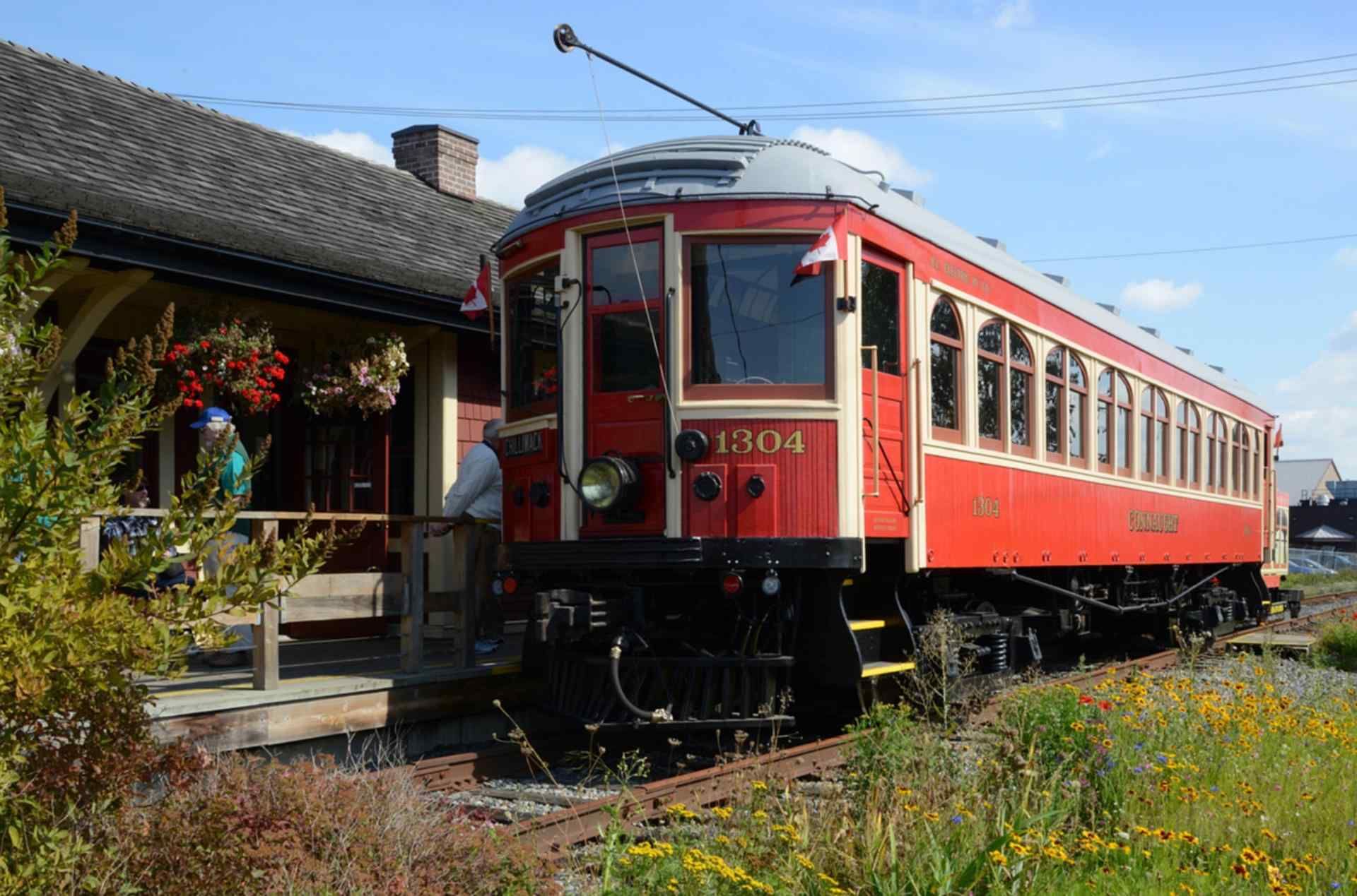 Red vintage railcar parked beside a station platform in a sunny outdoor setting