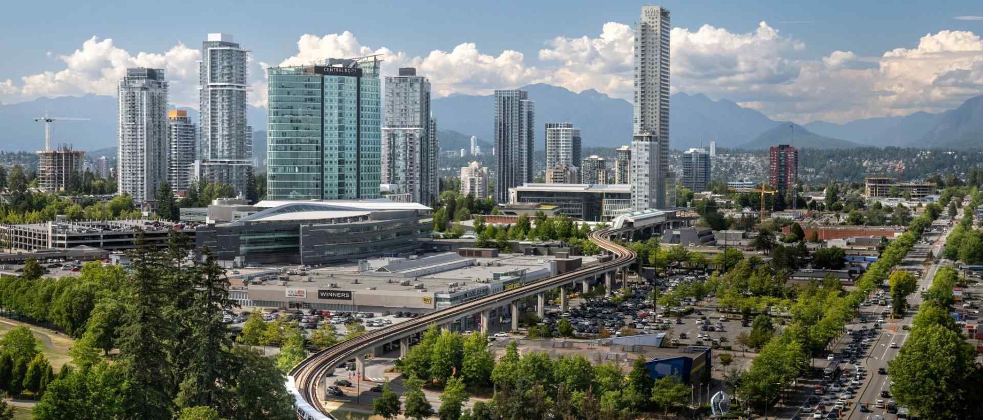 City skyline with modern high-rises, a central tower, and a busy roadway under a partly cloudy sky
