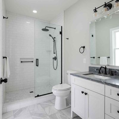 Bright white bathroom with glass shower, toilet, vanity, and large mirror.