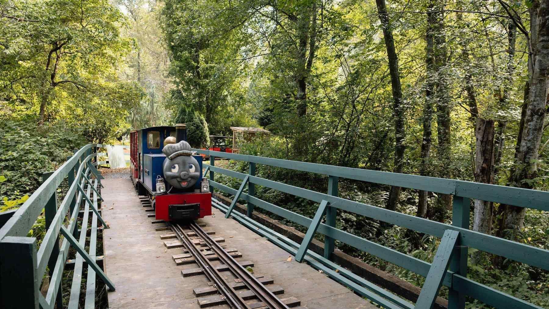 Small rail cart on tracks crossing a narrow blue bridge through a wooded area
