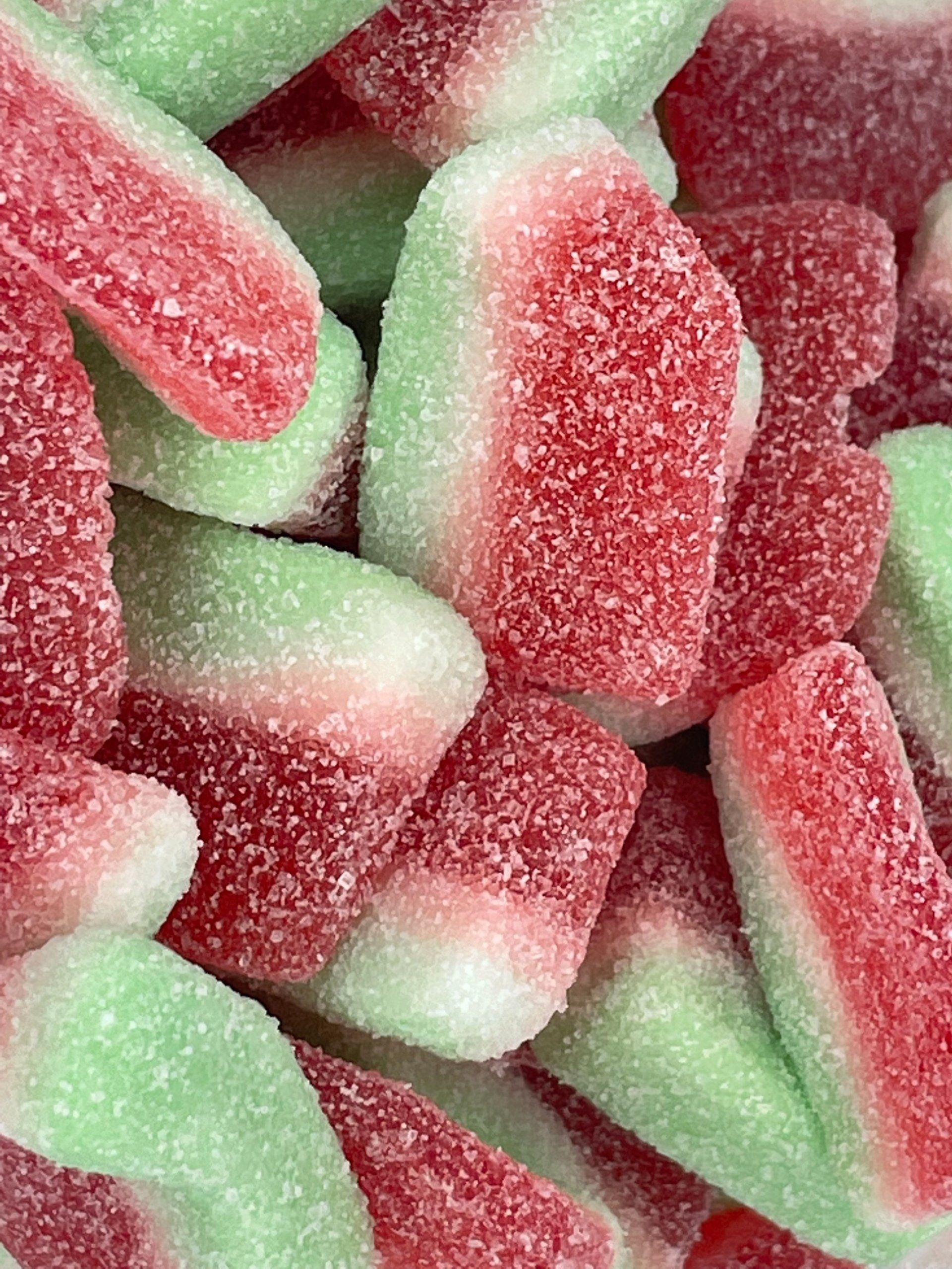 A close up of a pile of red and green gummy watermelons.