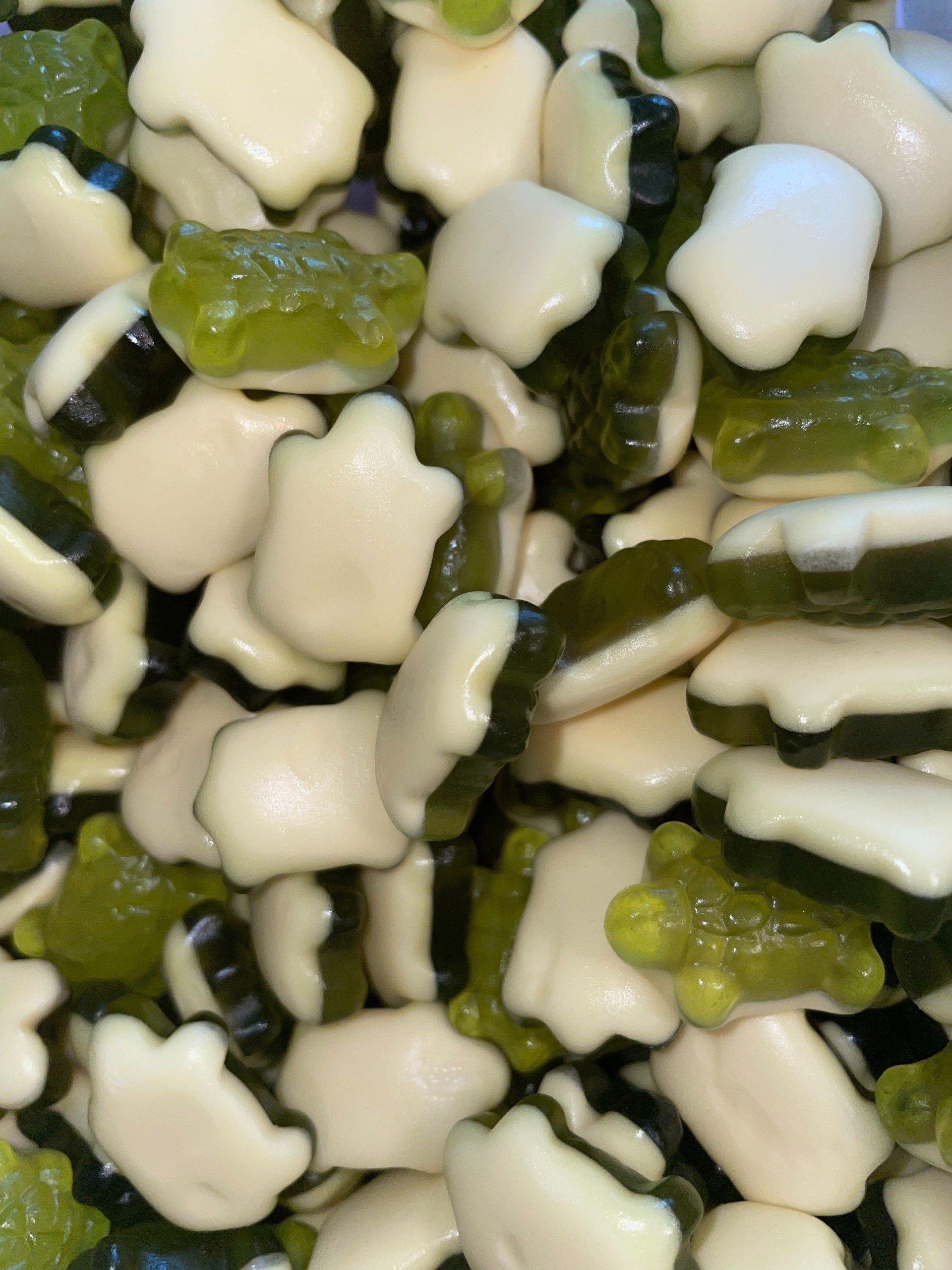 A pile of green and white gummy frogs