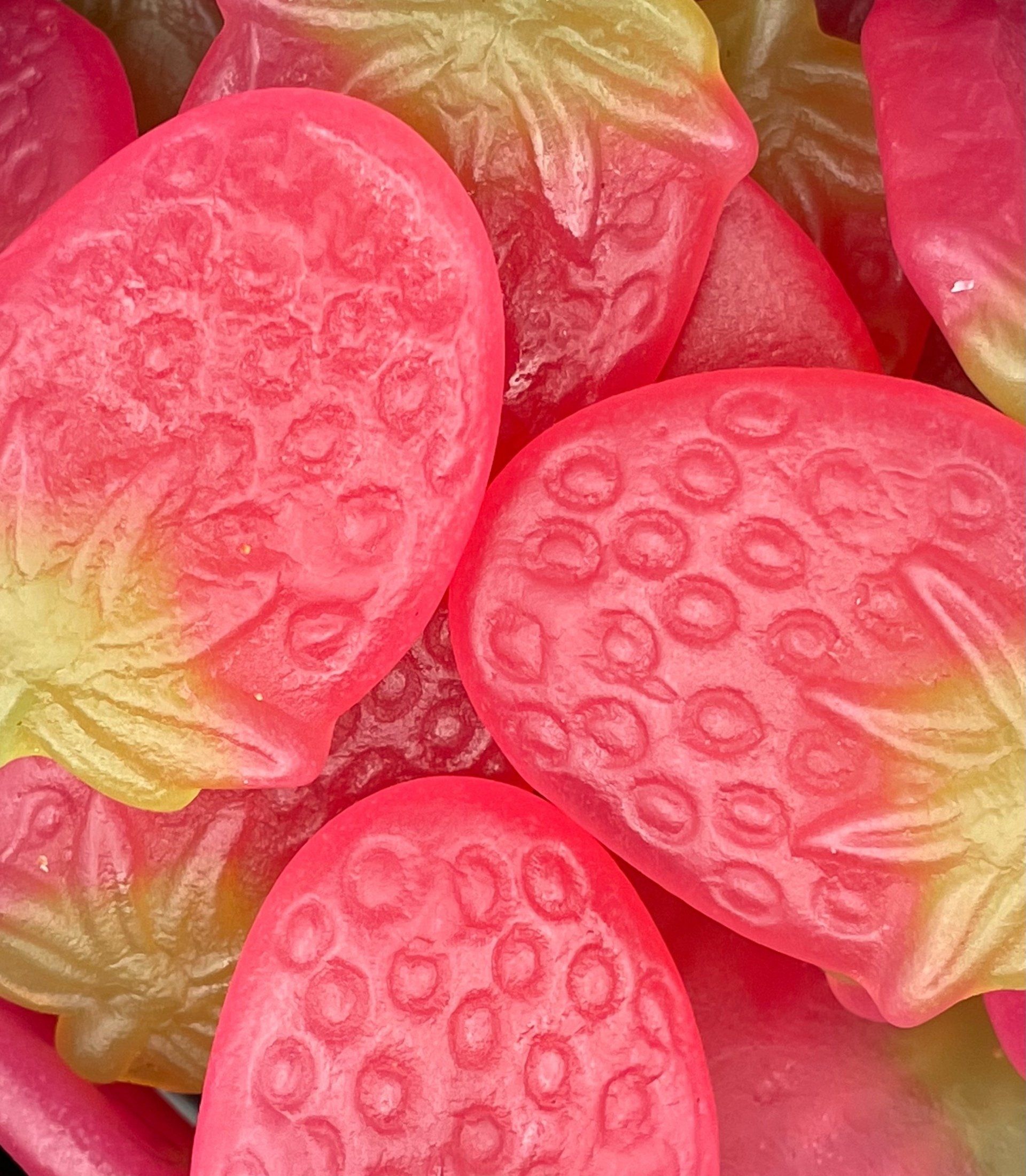 A close up of a pile of pink and yellow gummy strawberries.