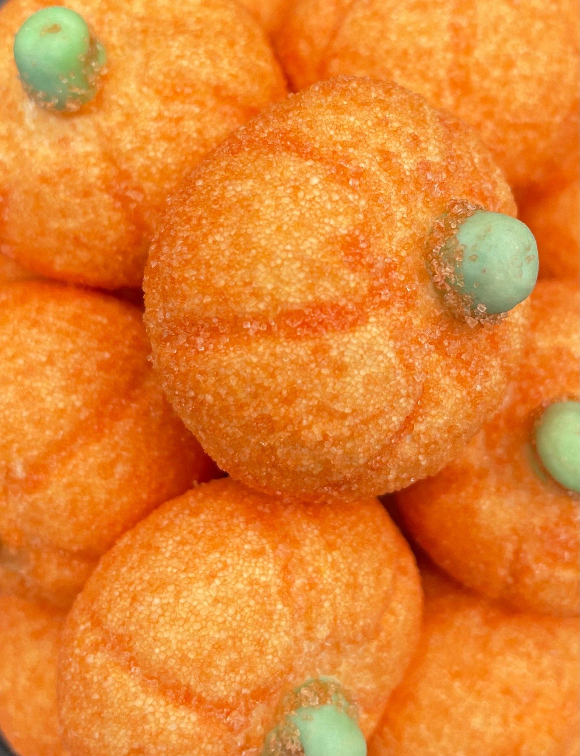 A close up of a pile of orange pumpkins with green stems.