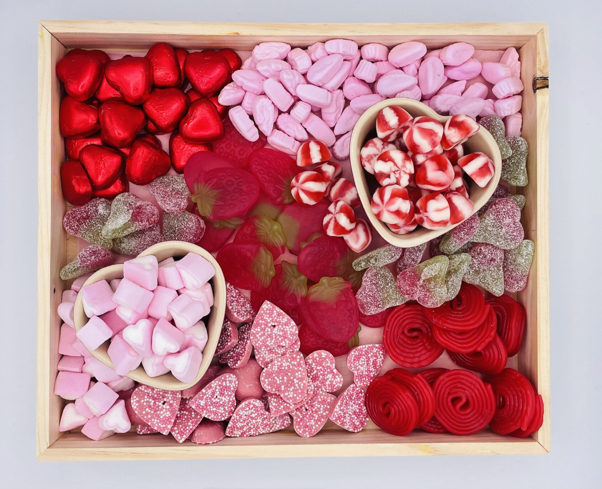 A wooden tray filled with a variety of pink and red candy.