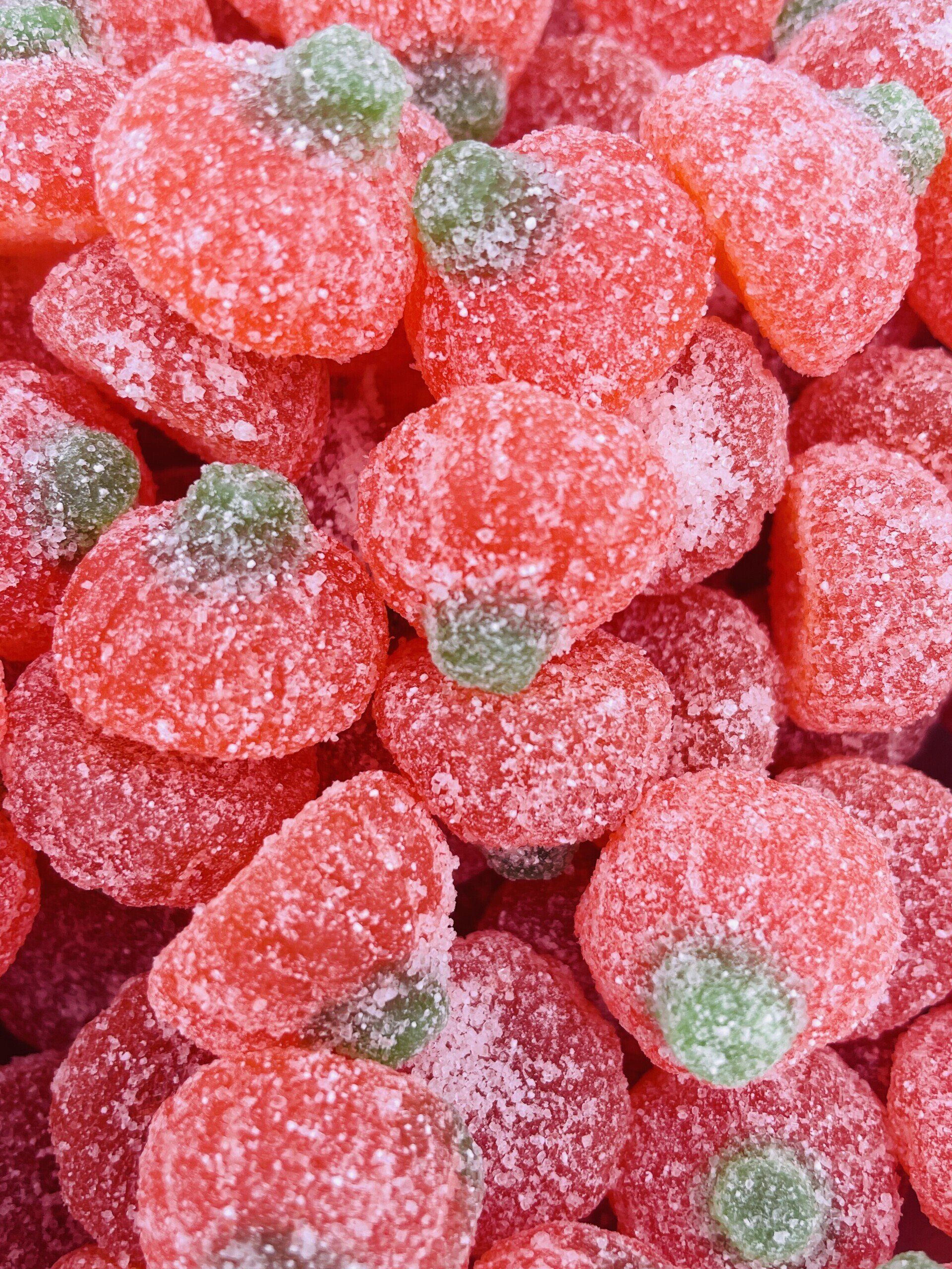 A pile of gummy strawberries with green stems covered in sugar.